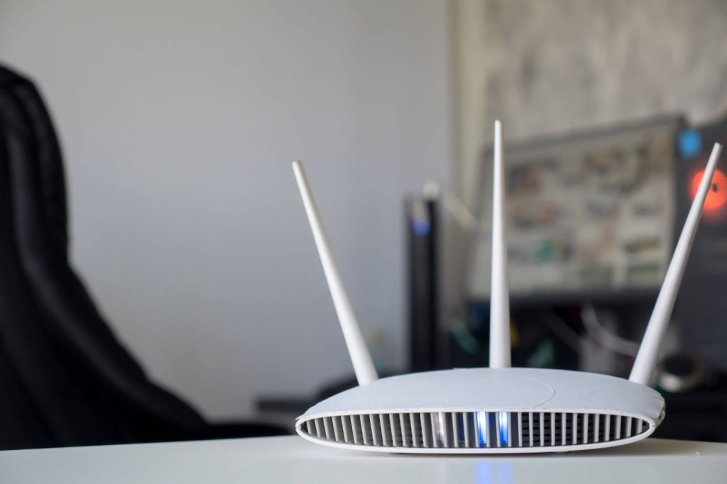 A white Wi-Fi router with blue lights on sits on a desk in a home office