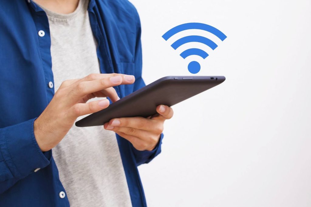A close-up of a person in a blue shirt using a digital tablet with a blue Wi-Fi signal icon floating above the screen