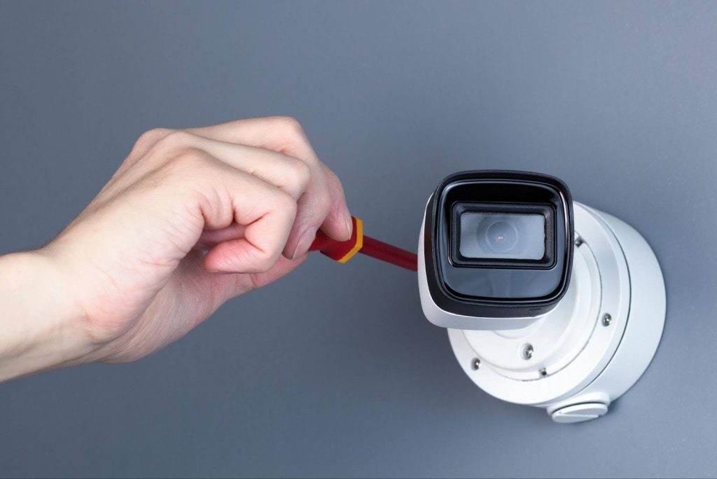 A technician's hand using a screwdriver to repair a mounted security camera to resolve why CCTV camera not working
